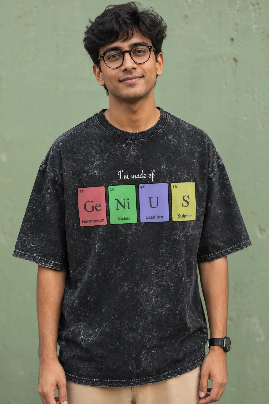 Person wearing a black t-shirt with colorful text design against a green wall.