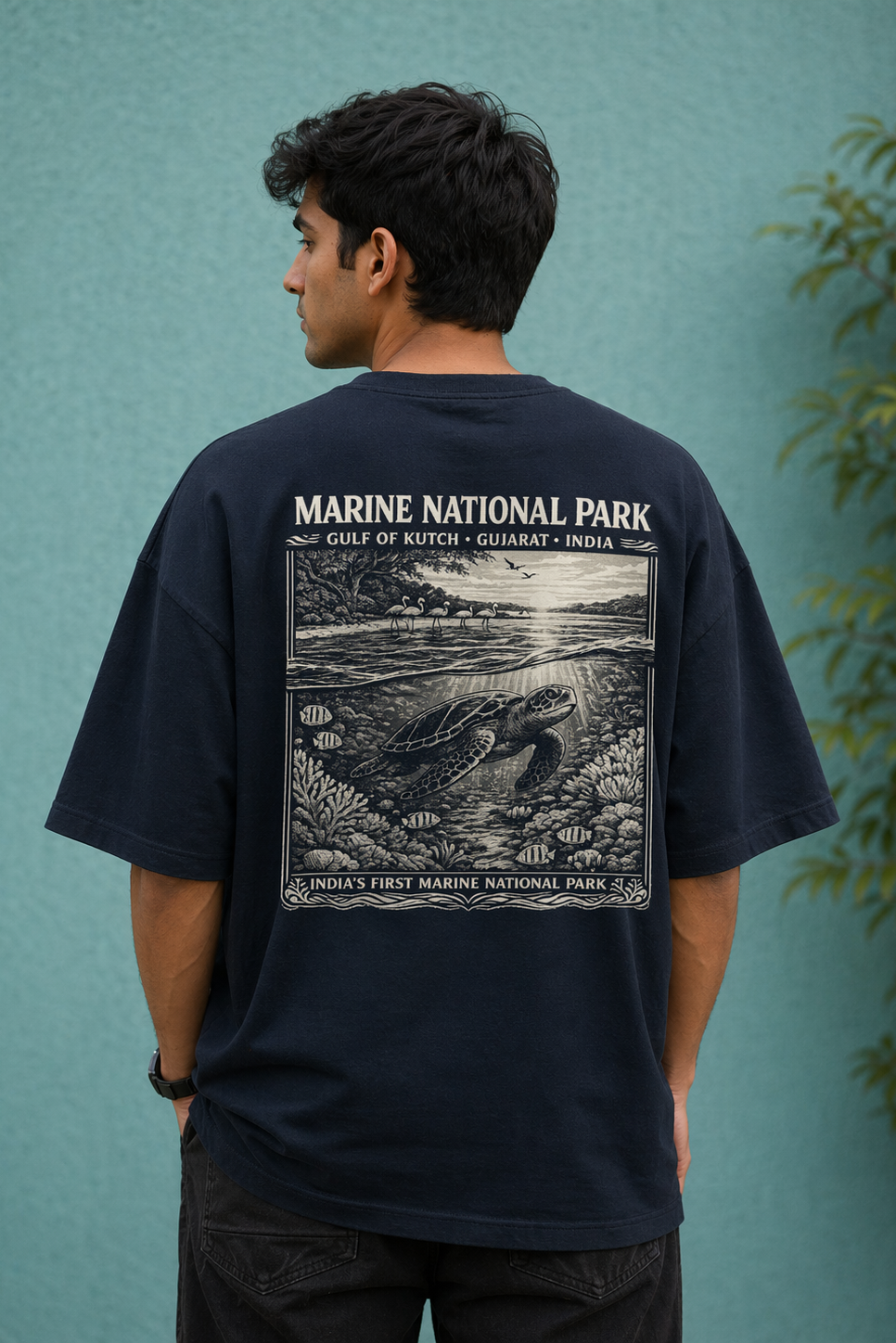 Person wearing a black t-shirt with 'Marine National Park' design on the back against a teal wall.